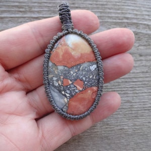 May include: A gray cord wrapped around a red, orange, and gray stone pendant. The stone has a marbled pattern.