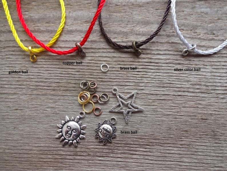 May include: A close-up of various cord colors and metal bails for jewelry making. The cords are red, yellow, brown, and white. The bails are gold, copper, and silver. There are also several jump rings and two charms: a sun and a star.
