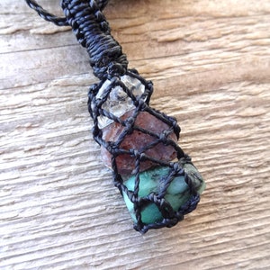 May include: A black cord necklace with a macrame knot holding three small stones. The stones are clear, brown, and green.