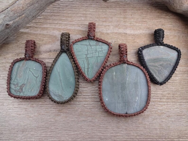 May include: Five pendants with different shaped stones, each wrapped in brown or black cord. The stones are green and have a marbled pattern.