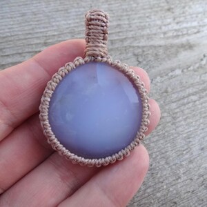 Peut inclure: Un pendentif rond en pierre pr&eacute;cieuse bleu clair avec un cordon en macram&eacute;. Le pendentif est d'un bleu doux et est entour&eacute; d'une bordure en macram&eacute; beige. Le cordon est &eacute;galement beige.