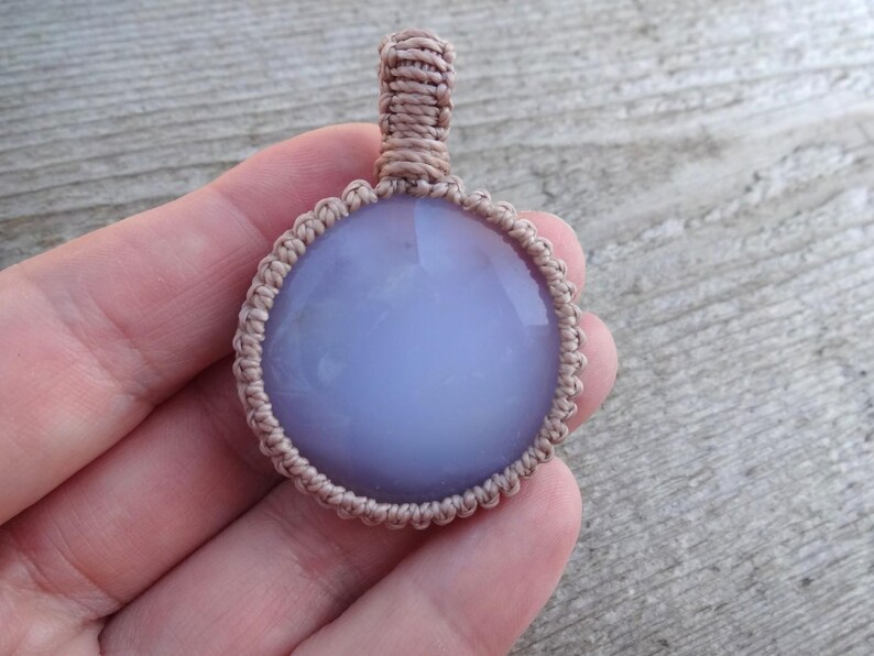 Peut inclure: Un pendentif rond en pierre pr&eacute;cieuse bleu clair avec un cordon en macram&eacute;. Le pendentif est d'un bleu doux et est entour&eacute; d'une bordure en macram&eacute; beige. Le cordon est &eacute;galement beige.