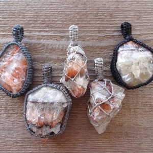 May include: Five gemstone pendants with a natural, earthy aesthetic. Each pendant features a raw, irregularly shaped crystal, encased in a woven macrame setting. The crystals display shades of orange, white, and clear, with the macrame in gray and black.
