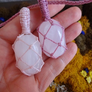 May include: Two white crystal stones wrapped in pink macrame cord. The stones are tied together with a pink cord.