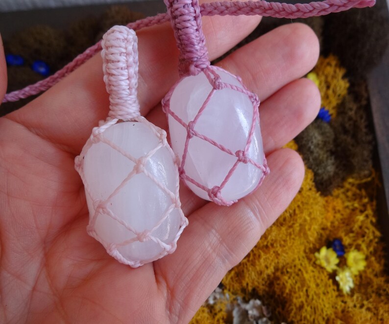May include: Two white crystal stones wrapped in pink macrame cord. The stones are tied together with a pink cord.