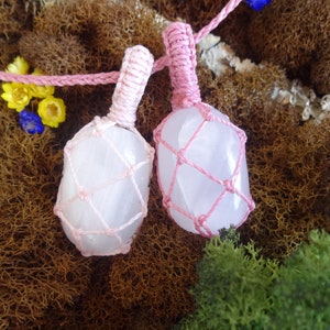 May include: Two pink crystal stones wrapped in pink macrame cord. The stones are smooth and have a light pink hue. The macrame cord is tied in a knot at the top of each stone.