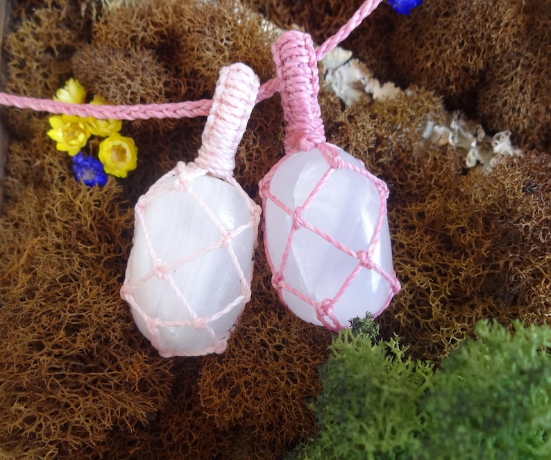 May include: Two pink crystal stones wrapped in pink macrame cord. The stones are smooth and have a light pink hue. The macrame cord is tied in a knot at the top of each stone.