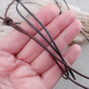 May include: A close-up of a brown and black leather cord necklace. The cord is knotted at the top and is held in a hand.
