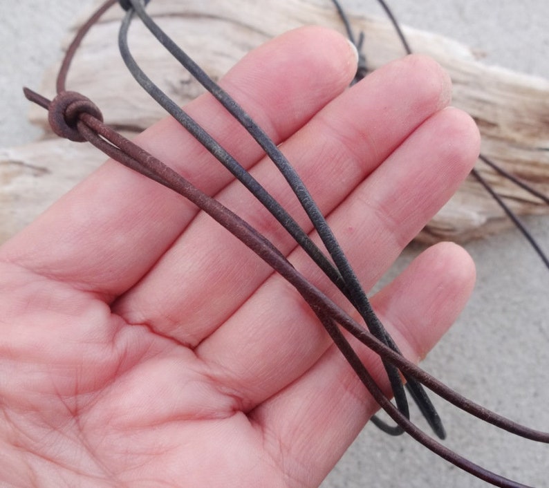 May include: A close-up of a brown and black leather cord necklace. The cord is knotted at the top and is held in a hand.