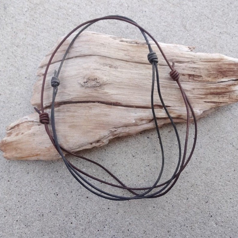 May include: Two leather cords with knots at the ends, one brown and one black, are displayed on a piece of driftwood.