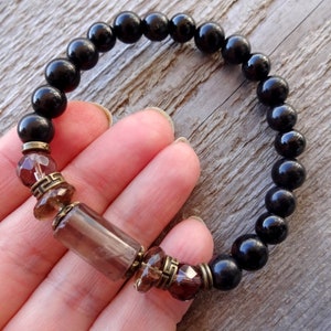 May include: Black beaded bracelet with brown and gold gemstone accents. The bracelet is made with round black beads and features a larger, rectangular brown gemstone with gold accents.