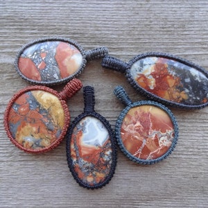 May include: Five oval-shaped pendants with a variety of red, brown, and gray marbled patterns. Each pendant is wrapped in a gray cord.