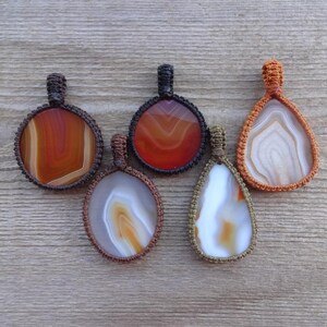 May include: Five agate stone pendants with different patterns and colors, each wrapped in a macrame cord. The pendants are in shades of brown, orange, and white.