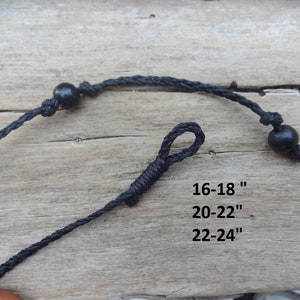May include: A black cord necklace featuring two round black beads and a knotted loop closure. The text printed on the image indicates available lengths of 16-18 inches, 20-22 inches, and 22-24 inches for this adjustable cord necklace design.