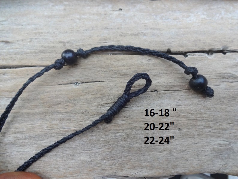May include: A black cord necklace featuring two round black beads and a knotted loop closure. The text printed on the image indicates available lengths of 16-18 inches, 20-22 inches, and 22-24 inches for this adjustable cord necklace design.