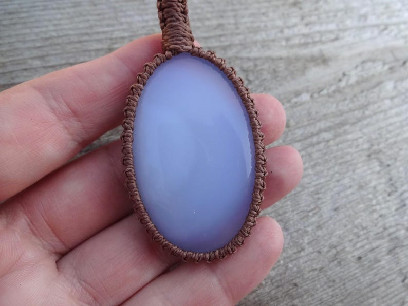 Peut inclure: Pendentif en pierre pr&eacute;cieuse ovale bleu clair, serti dans un tissage macram&eacute; marron. Le pendentif a une surface lisse et polie et un aspect translucide. Le cordon macram&eacute; est finement tiss&eacute; autour de la pierre.
