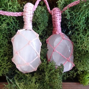 May include: Two pink crystal pendants wrapped in pink macrame cord. The crystals are clear and have a slight pink hue. The pendants are hanging from a pink cord.