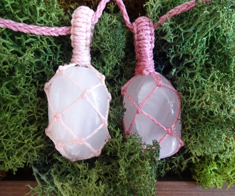 May include: Two pink crystal pendants wrapped in pink macrame cord. The crystals are clear and have a slight pink hue. The pendants are hanging from a pink cord.