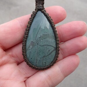 May include: A green and brown stone pendant with a unique pattern, set in a brown leather cord.