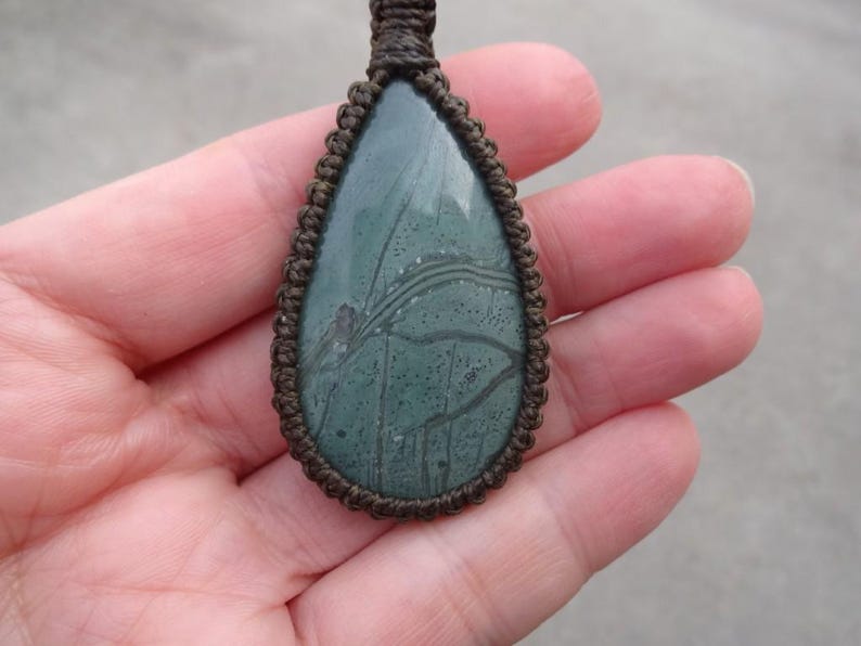 May include: A green and brown stone pendant with a unique pattern, set in a brown leather cord.