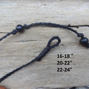 May include: Close-up of a black necklace with adjustable length. The necklace features a knotted design with a wooden bead and a loop closure. Text on the image indicates lengths of 16-18", 20-22", and 22-24".