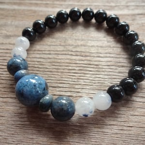Op de afbeelding: Een armband met zwarte, witte en blauwe kralen. De armband heeft een grotere blauwe kraal in het midden.