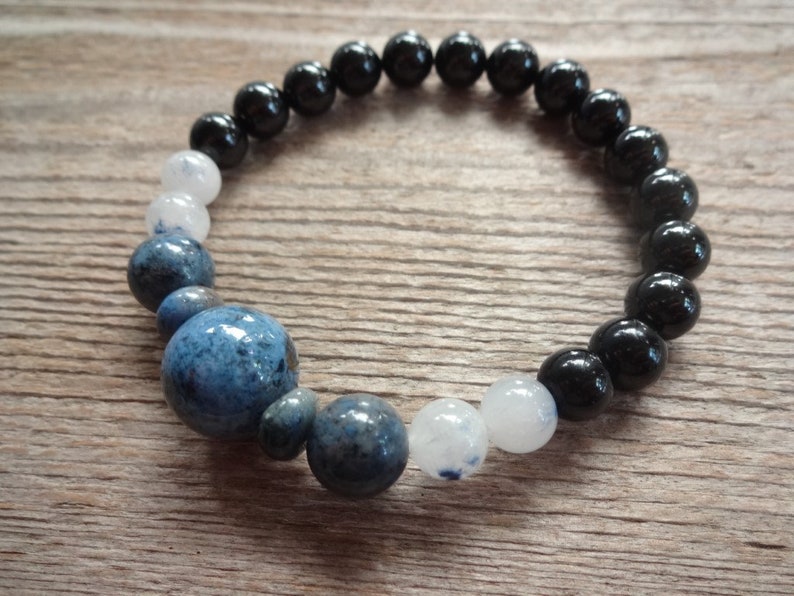 Op de afbeelding: Een armband met zwarte, witte en blauwe kralen. De armband heeft een grotere blauwe kraal in het midden.