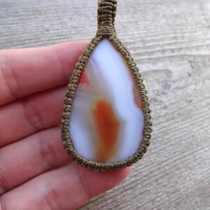 May include: A white agate pendant with orange and red markings, wrapped in brown cord.