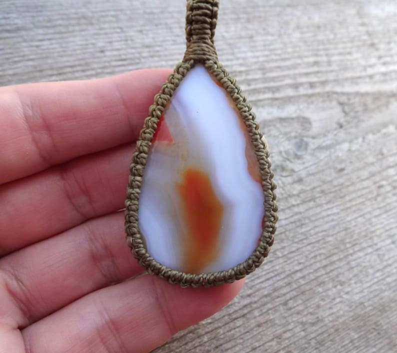 May include: A white agate pendant with orange and red markings, wrapped in brown cord.