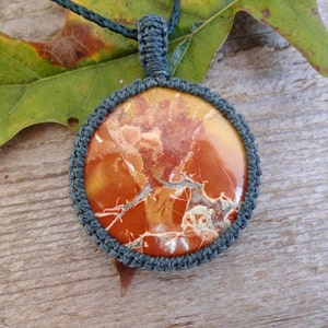 May include: A round, red, orange, and white jasper stone pendant with a gray macrame cord.