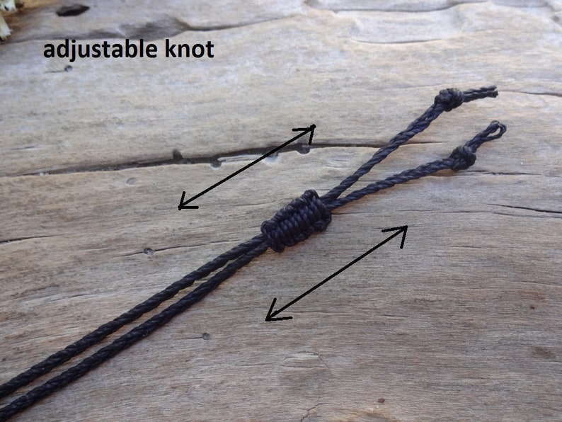 May include: A black cord featuring an adjustable knot mechanism. The cord is composed of two strands that pass through a central sliding knot, allowing for length modification. The text "adjustable knot" is visible in the upper left corner.