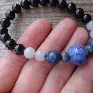 Op de afbeelding: Een armband met zwarte, witte en blauwe kralen met een grote blauwe kraal in het midden.