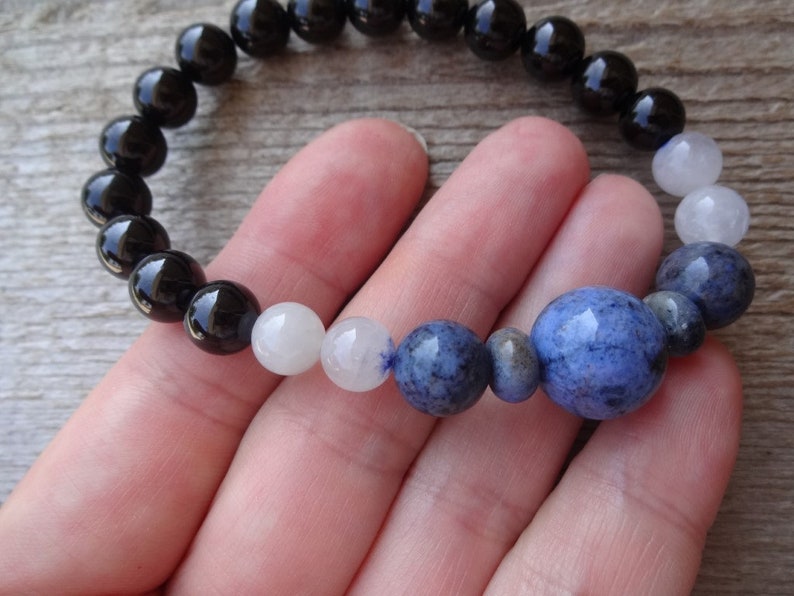 Op de afbeelding: Een armband met zwarte, witte en blauwe kralen met een grote blauwe kraal in het midden.