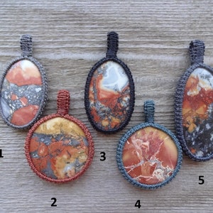 May include: Five oval-shaped pendants with different patterns of red, orange, brown, white, and black. Each pendant is surrounded by a gray or blue cord.