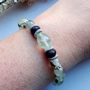 May include: A green and black beaded bracelet with silver accents. The bracelet is made of natural stones and is worn on a person's wrist.