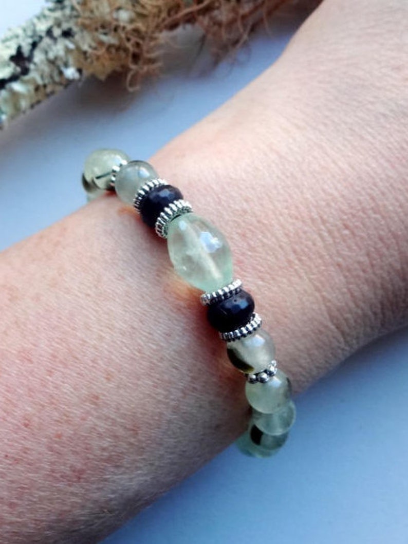 May include: A green and black beaded bracelet with silver accents. The bracelet is made of natural stones and is worn on a person's wrist.