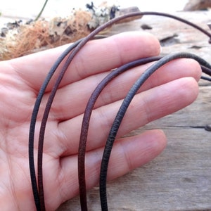 May include: Three leather cords in different colors: black, brown, and dark brown. The cords are shown in a hand, with the ends of the cords visible.