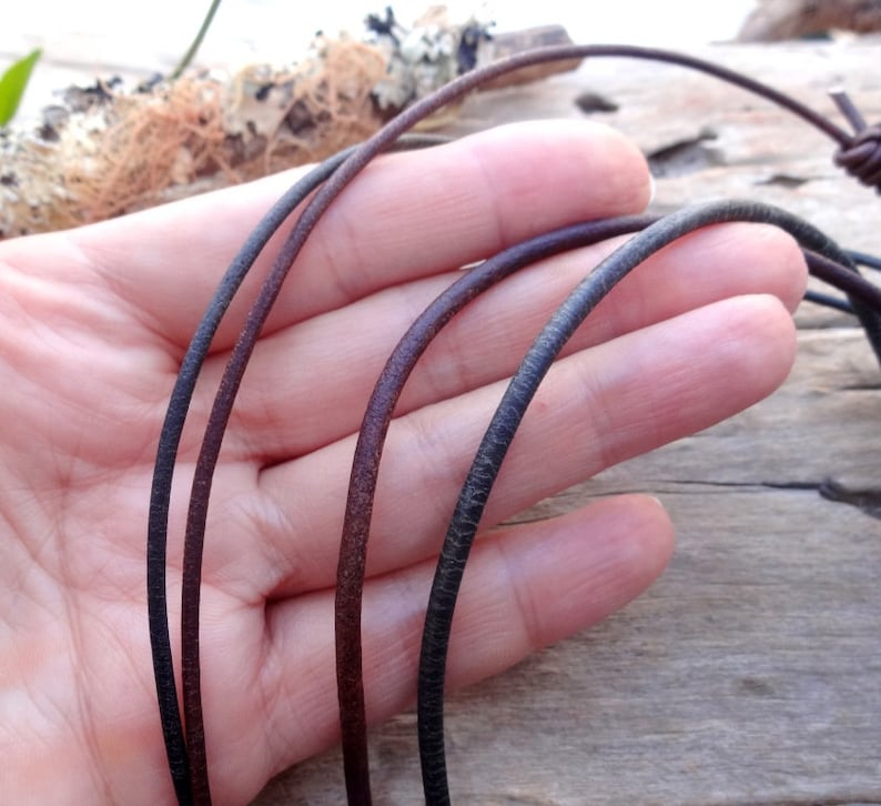 May include: Three leather cords in different colors: black, brown, and dark brown. The cords are shown in a hand, with the ends of the cords visible.
