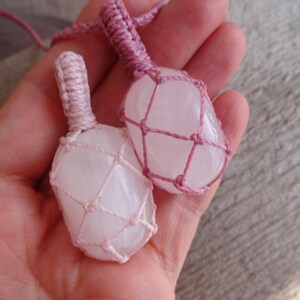 May include: Two pink crystal stones are wrapped in pink macrame cord. The stones are smooth and have a natural, cloudy appearance.