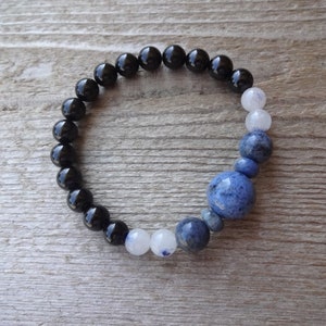 Op de afbeelding: Een armband met zwarte, witte en blauwe kralen met een grote blauwe edelsteen in het midden.