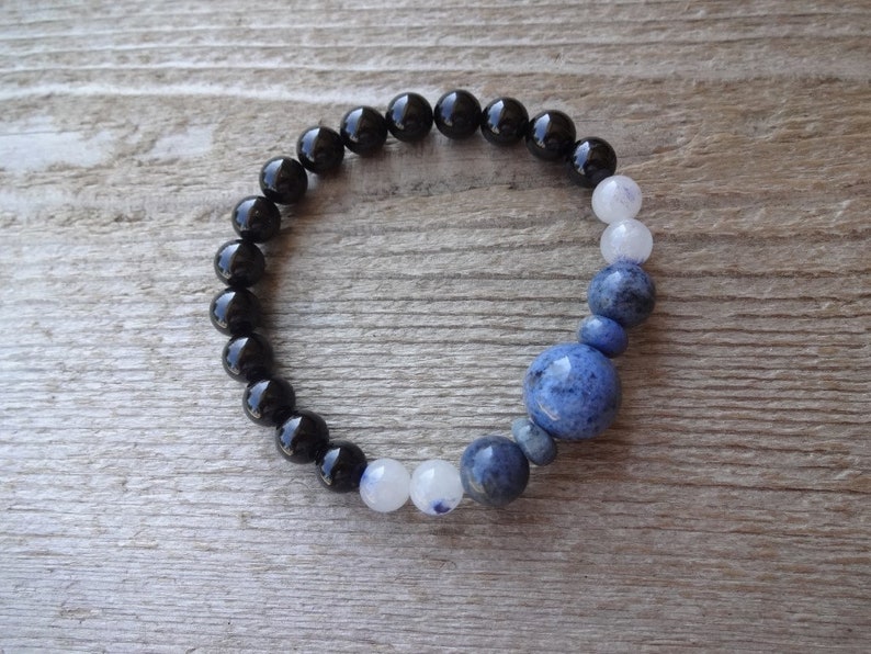 Op de afbeelding: Een armband met zwarte, witte en blauwe kralen met een grote blauwe edelsteen in het midden.
