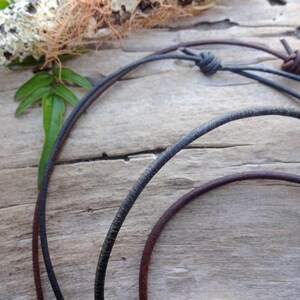 May include: Two leather cords, one black and one brown, are tied together with a knot. The cords are lying on a wooden surface.