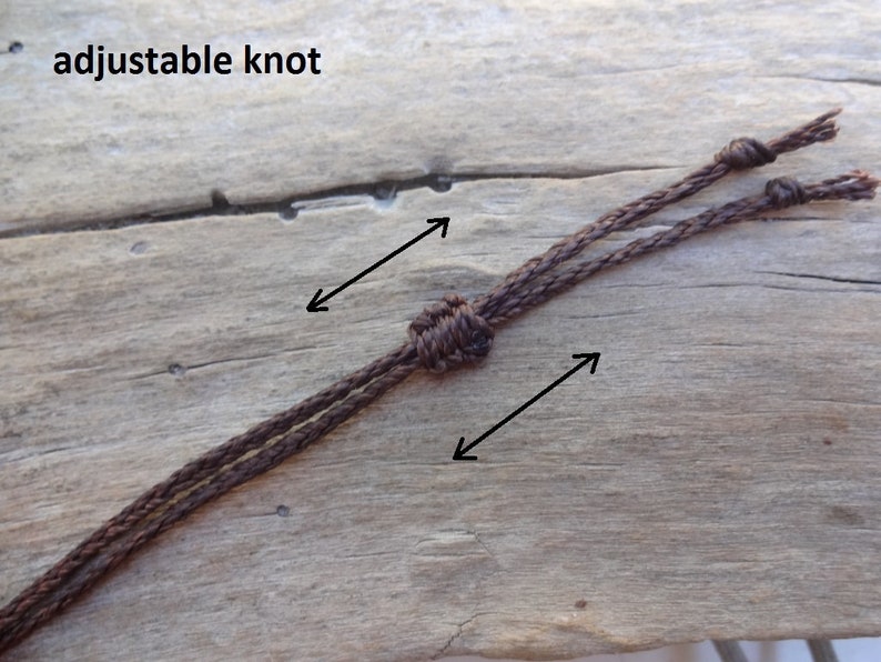 May include: Close-up of a brown cord with an adjustable knot. The text "adjustable knot" is visible at the top of the image. The cord is made of a woven material and is set against a wooden background.