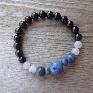 Op de afbeelding: Een armband van zwarte onyx en blauwe lapis lazuli kralen met een grotere lapis lazuli kraal in het midden.