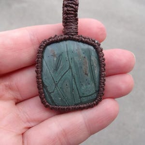 May include: A green and brown stone pendant with a unique pattern, set in a brown macrame cord.