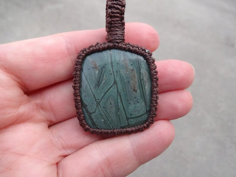 May include: A green and brown stone pendant with a unique pattern, set in a brown macrame cord.