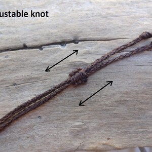 May include: A close-up of a brown cord with an adjustable knot. The cord is tied with two knots, one at each end. The text "adjustable knot" is written in black letters at the top of the image.