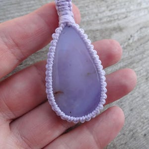Peut inclure: Pendentif en forme de goutte d'eau avec une pierre violet clair, entour&eacute; d'un motif macram&eacute;. Le pendentif est suspendu &agrave; un cordon assorti. La pierre a une surface lisse et est de couleur lavande.
