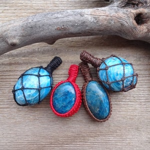 May include: Four blue apatite crystal pendants wrapped in different colored cords. The cords are black, red, and brown. The crystals are all different shapes and sizes.