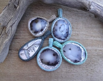 May include: Five agate pendants with different patterns and colors, each wrapped in a macrame cord. The pendants are displayed on a wooden surface.